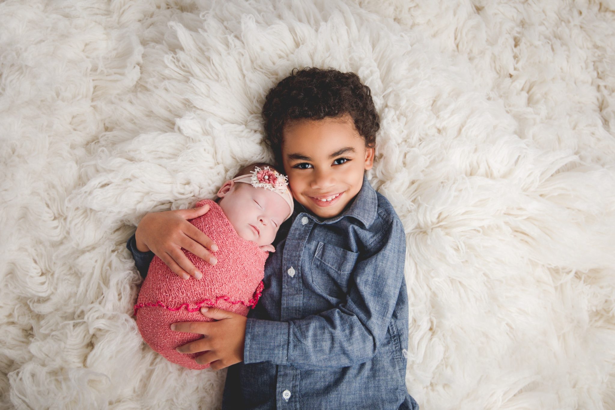 Newborn and sibling love on classic white fur background.