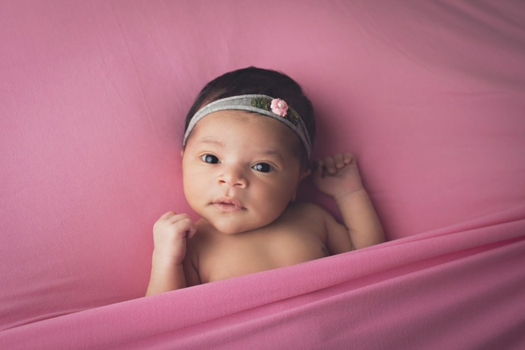 Newborn baby girl lying on pink blanket with eyes open