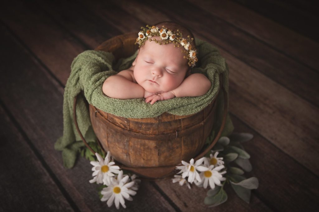 Newborn baby girl photographed in a wooden bucket with daisy floral crown