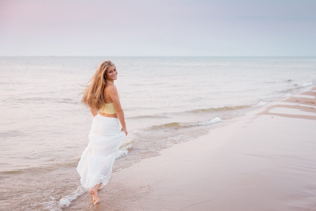 High school senior girl in a skirt skipping on the water's edge of Lake Michigan in Saint Joseph Michigan